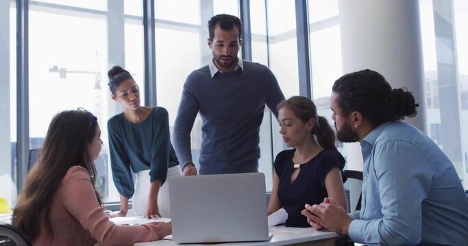 Leading leader standing behind laptop guiding team in modern meeting room, wearing business-casual