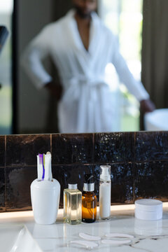 Toothbrushes and skincare pumps are sitting on marble vanity countertop near dark tile backsplash