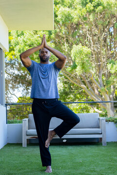 Mature African man practicing yoga on terrace wearing gray tee black pants barefoot near sofa