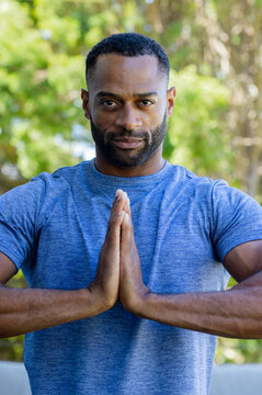African American mature male holding hands in prayer at chest outdoors wearing blue athletic shirt