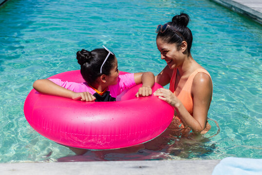 African American mother and teen daughter in swimsuits playing in pool with pink ring and goggles
