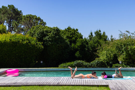 African woman, teenage girl lounging in swimwear on towels at pool with pink ring, copy space