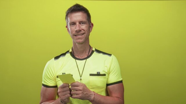 Man referee holding yellow card and whistle in studio set against lime green; confidence fairness authority.