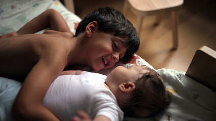 Young boy lying down next to baby sibling, gentle bonding moment, brother looking at infant with...