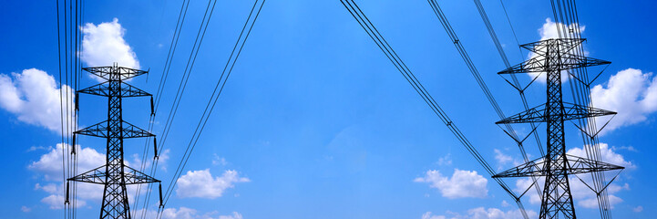 Electric towers and high-voltage lines stretch across a bright blue sky, with some fluffy clouds enhancing the overall aesthetic.