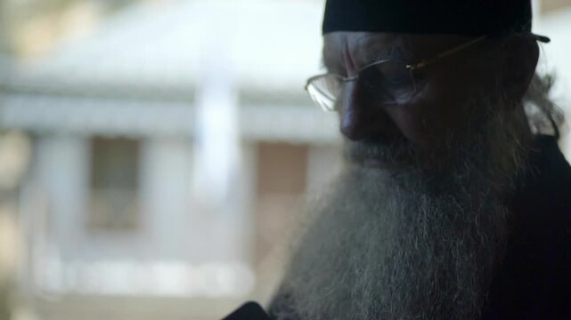 Elderly orthodox monk with long beard holding and looking at his cellphone in Mount Athos, Greece