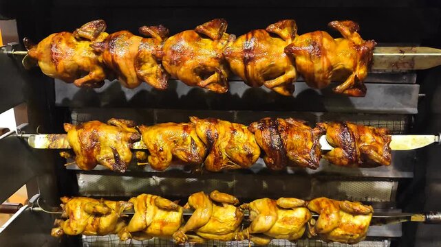 Row of golden brown whole roasted chickens rotating on a professional rotisserie spit. Close-up of juicy, crispy chicken in a commercial oven.