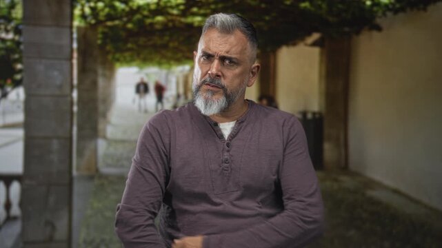 Man with gray beard pointing index finger toward camera in building entrance by house doorway outdoors; stern warning.