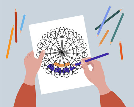 Coloring a coloring page, top-down view showing hands, pencils and mandala coloring image.