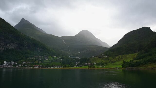 Bergige Landschaft mit einem ruhigen Fjord, in dem die umliegenden Berge und das Dorf reflektiert werden, umgeben von gr&uuml;ner Natur, Geirangerfjord, Geiranger, Stranda, Romsdal, Norwegen, Europa