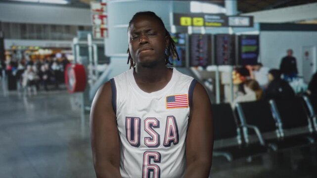 Man wearing usa basketball jersey biting his lip and closing eyes in an airport terminal; impatience travel delay.
