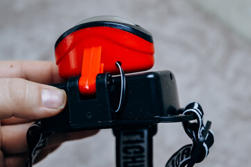 Close-up of a headlamp held in hand. Portable LED flashlight with adjustable strap for outdoor...