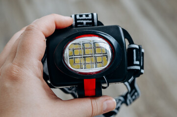 Fototapeta premium Close-up of a headlamp held in hand. Portable LED flashlight with adjustable strap for outdoor activities, camping, hiking and hands-free lighting in low light conditions.