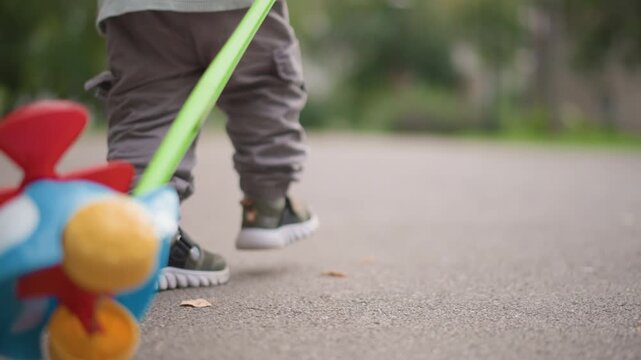 White toddler pulling colorful airplane toy, toddler practicing walking across pavement with pull toy, small strides and determined gait, sneakers scuffing ground, playful independence and exploration