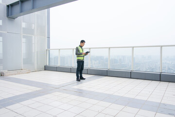 Engineer inspecting equipment on rooftop while holding a tablet device during daytime © zhu difeng