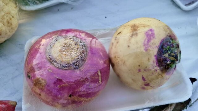 Purple-top turnips (Brassica rapa subsp. rapa) wrapped in plastic on a tray, with moisture droplets visible, displayed as freshly harvested root vegetables.