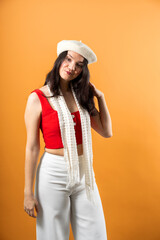 Naklejka premium Young woman posing in a studio wearing a beret, red top, and white pants