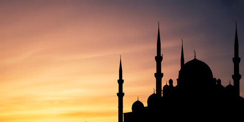 Fototapeta premium Silhouette of a mosque with minarets at sunset or sunrise with orange sky