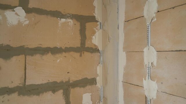 Close-up video of a construction site. A camera moves along a new block wall, showing the preparation steps before applying plaster, including beacons and corner beads.