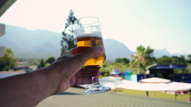 Pov of hand holding glass of beer man on vacation drinks cold and fresh beverage, relaxing and enjoying summer time.