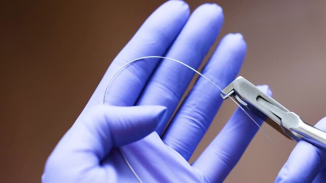 Extreme close up of orthodontist using pliers to handle thin archwire during braces adjustment. Gloved hands demonstrate precise control and careful fixation of orthodontic wire in clinical setting.
