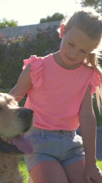 Vertical video: Reaching child petting dog in yard rising and showing love in pink top denim shorts