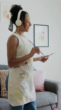 Vertical video: Putting brush to canvas, apron painter painting to relax at home, easel palette