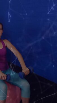 Vertical video: Woman on ball holding DBs, clip starting nodes over face and UI sliding for fitness