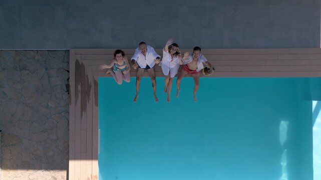 Aerial view of adult friends relaxing next to outdoor pool waving to camera.