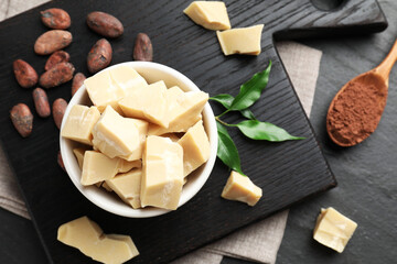 Organic cocoa butter, beans, powder and green leaves on black table, flat lay