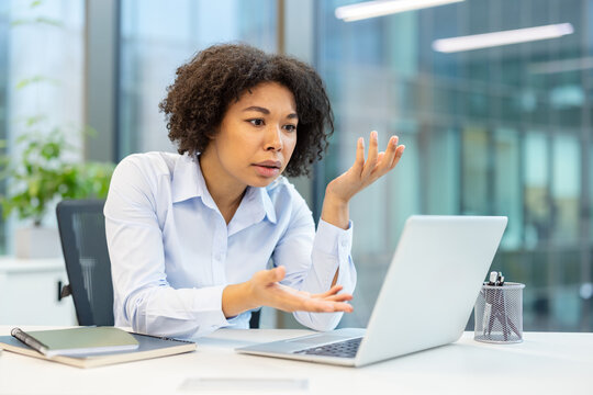 Dissatisfied young African American woman talking on video call on laptop in office