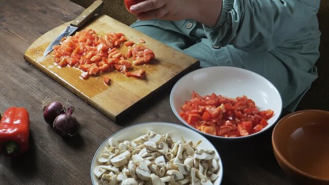 Slicing fresh tomatoes with a knife on a cutting board on a wooden table. Medium shot.
