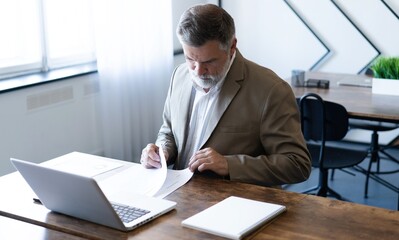 Fototapeta premium Mature businessman working with document in modern office, reading contract, analyzes graph