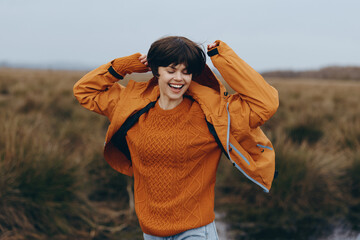 Happy woman lifestyle concept outdoors in autumn field wearing orange sweater and jacket, smiling...