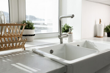 Modern sink with water tap near window in kitchen, closeup. Interior design