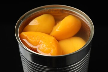 Pickled peaches in tin can on black background, closeup