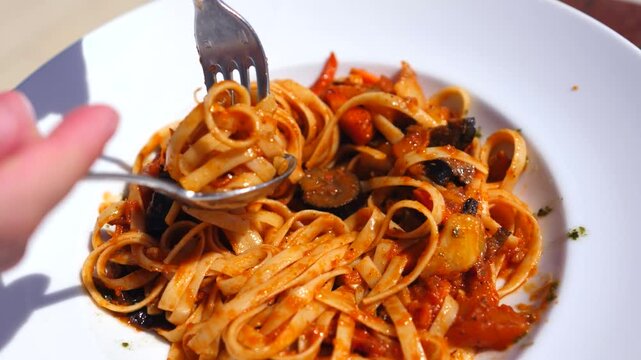 Delicious italian fettuccine pasta with vegetable sauce being rolled with a fork and spoon in a white plate. Fresh and healthy vegetarian meal ready to be eaten for lunch or dinner in a restaurant