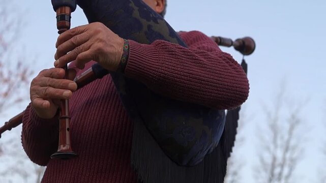 A detailed shot focusing on the hands and fingers of an elderly musician skillfully playing the chanter of a wooden bagpipe.