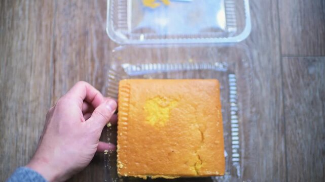 Square cornbread slice in plastic container with sale reduced price label sign, hand opening cover lid showing corn bread food