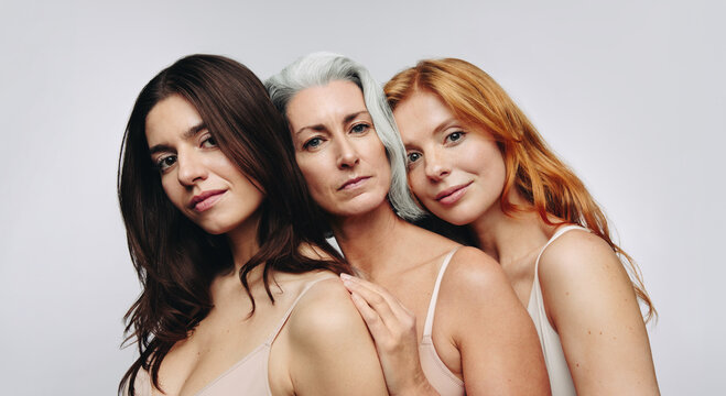 Three women embrace in studio gentle pose brunette gray and redhead