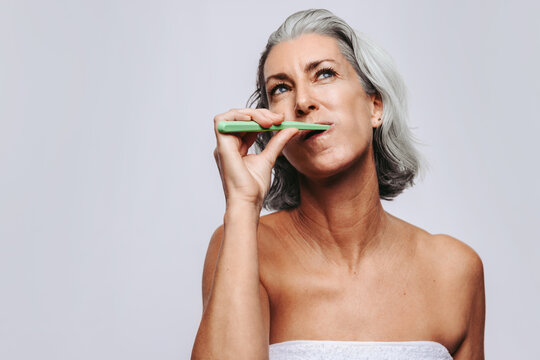 Mature woman in her 50s brushing teeth in studio