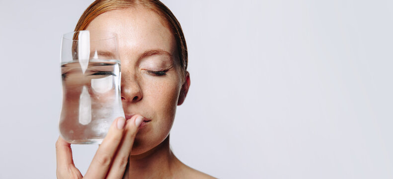 Woman holding glass of water to her face eyes closed