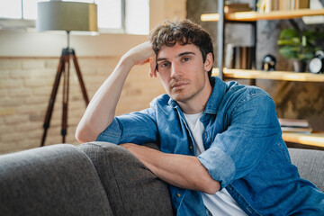 Fototapeta premium Man, serious and portrait in living room of home, relax with pride and good mood on day off or weekend break. Proud, confidence and male person for holiday at house and chill on sofa