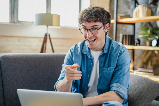 Gesture, video call and laptop with man on sofa for freelancer, networking and welcome. Greeting, communication and remote worker with person in living room of home for small business and streaming