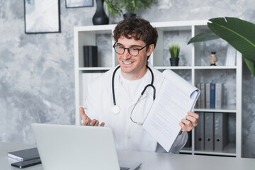 Obraz premium Online medical consultation. Confident male doctor family therapist sit by laptop talk to patient via telehealth videocall explain diagnosis give recommendations remotely from clinic office