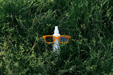 Bright orange glasses resting on a plastic spray bottle on green grass. Creative minimal outdoor composition