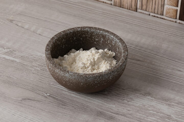 Bowl containing flour placed on a wooden surface in a kitchen setting with natural light