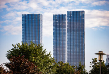 Obraz premium Modern architecture with glass skyscrapers rising above green park trees