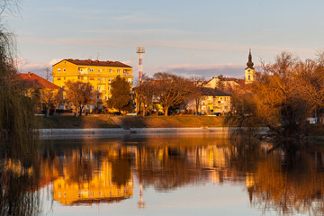 Obraz premium Golden Hour Church and Clock Tower Reflection Over Quiet River in Small Town Landscape, Vinkovci, Croatia