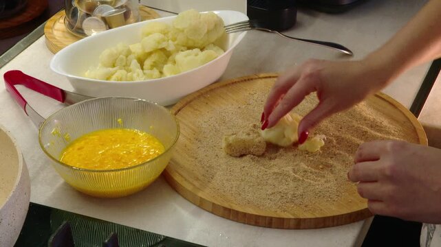 Woman breading cauliflower with egg and breadcrumbs